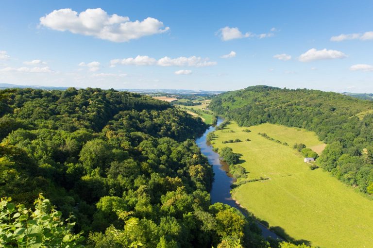 Looking down the river Wye with green fields and green forest. 