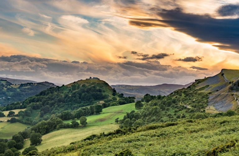 Looking across Eglwyseg Crag and on to the town of Llangollen, with green mountains and sunset sky.